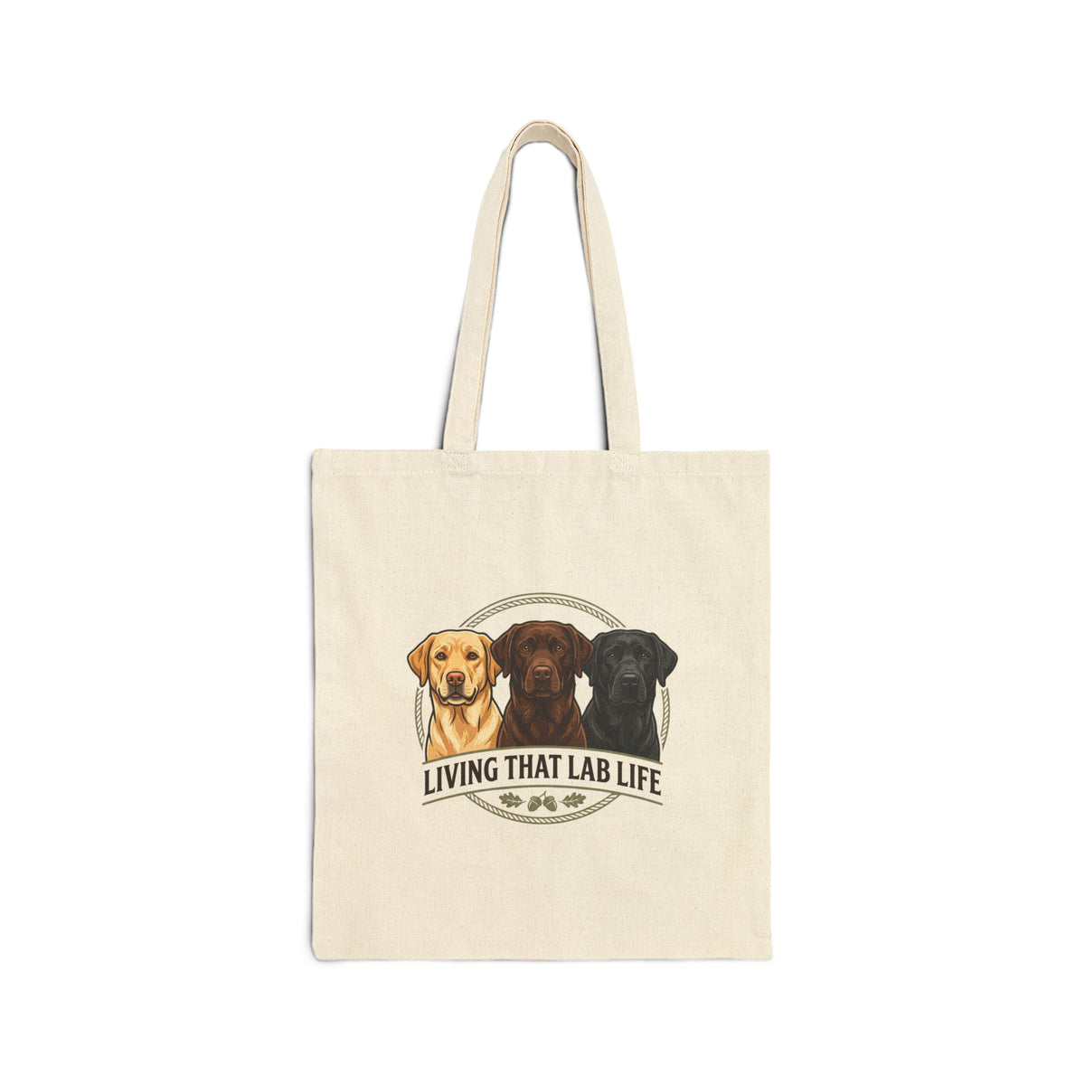 An off-white canvas tote bag with two shoulder straps, featuring a graphic print of three Labrador Retriever portraits in yellow, brown, and black, with the text 'LIVING THAT LAB LIFE' and paw prints below.