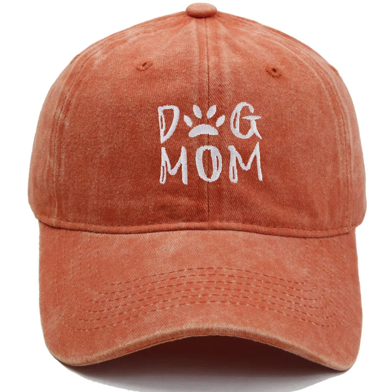 A washed terracotta orange baseball cap featuring the words 'DOG MOM' embroidered in white on the front, with a paw print detail inside the letter 'O'.