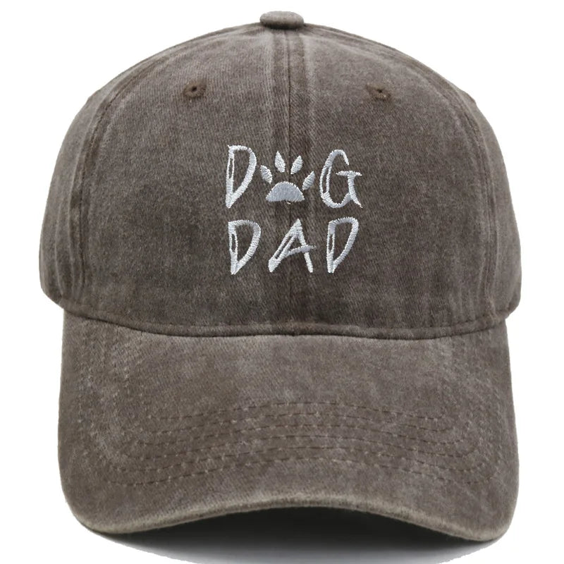 A washed dark gray baseball cap featuring 'DOG DAD' embroidered on the front, with a paw print graphic inside the letter 'O'.