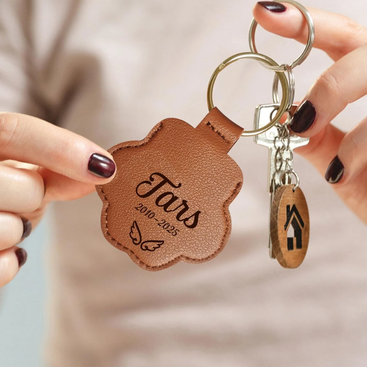 Brown leather keychain with engraved text held by a person against a neutral background