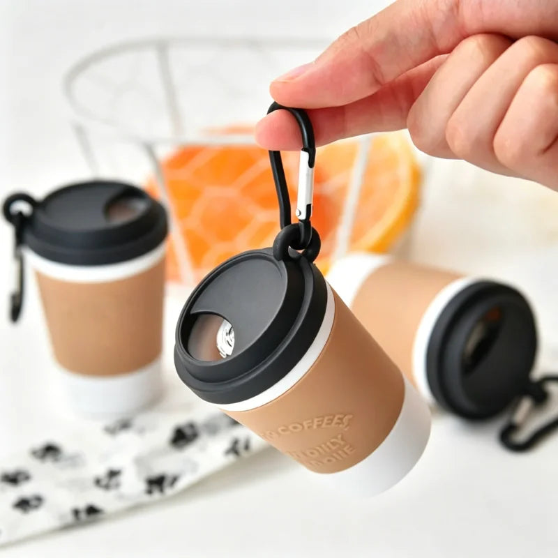Reusable coffee cup with black lid and carabiner, held by a hand.