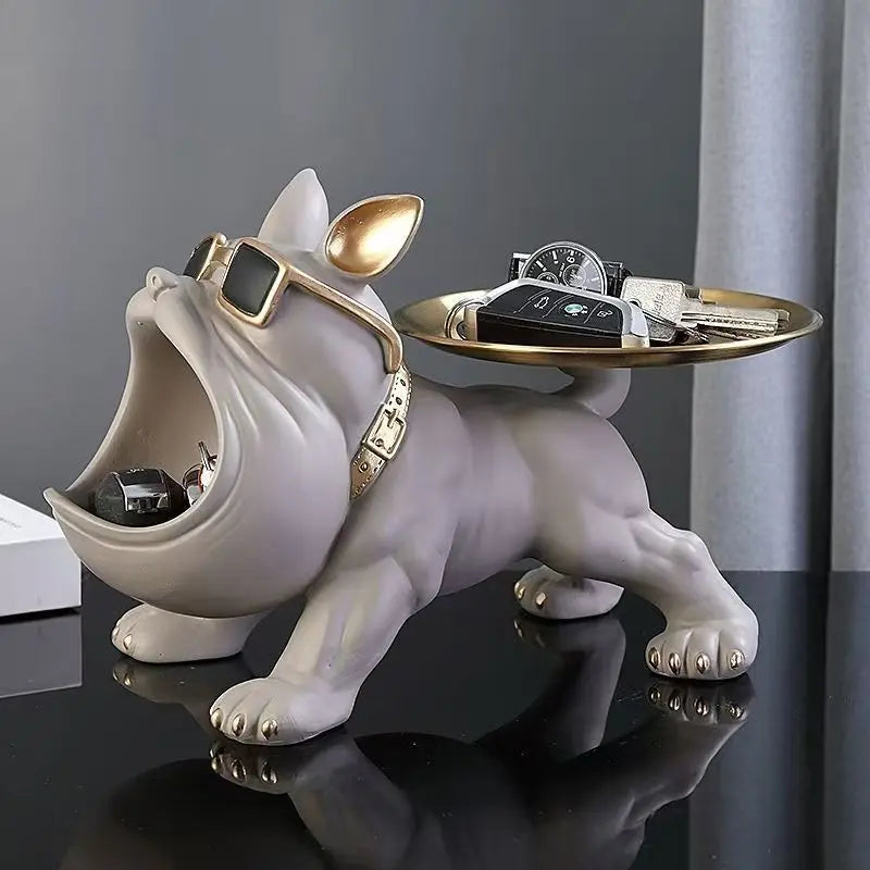 A sculptural dog-shaped jewelry organizer and tray holder in a glossy off-white finish, accessorized with gold sunglasses and a gold collar. The open mouth contains a small black car model, and a round gold tray on its back holds keys and a watch.