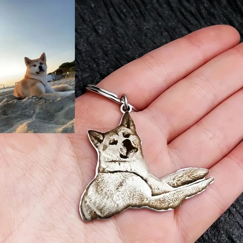 Silver dog-shaped keychain held in a hand with a split image of a dog on a beach.