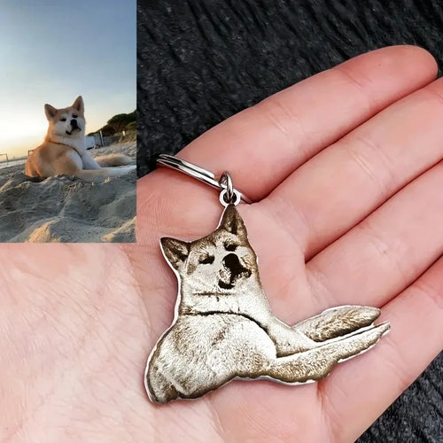 Silver dog-shaped keychain held in a hand with a split image of a dog on a beach.