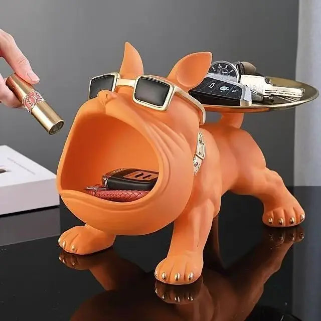 An orange dog-shaped desk organizer with sunglasses, shown holding keys and a lipstick tube being held by a hand. The dog has a tray on its back holding car keys and a watch.